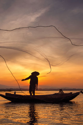 A fisherman in Myanmar throws their net at sunrise