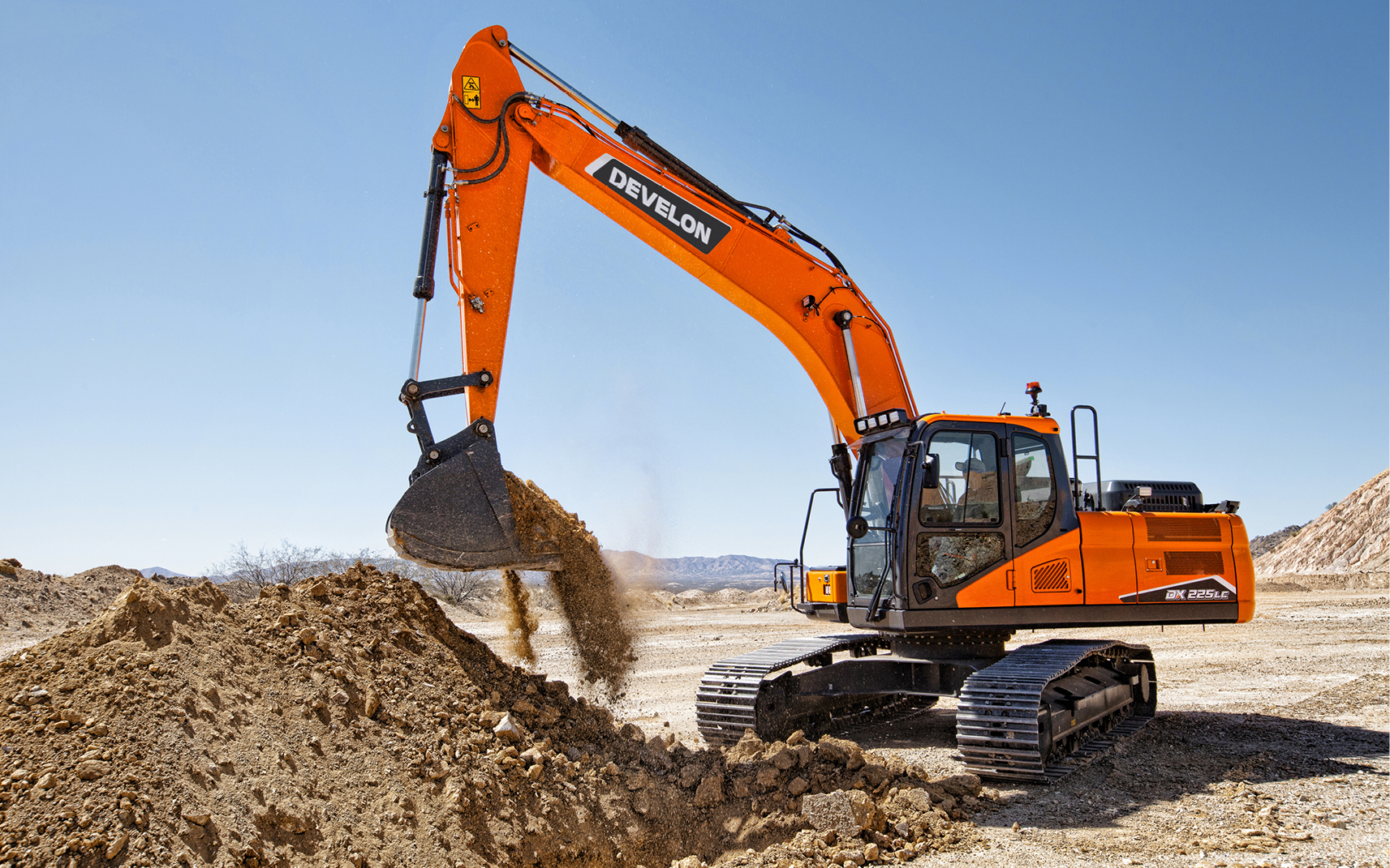 A DEVELON crawler excavator working with a large pile of dirt.