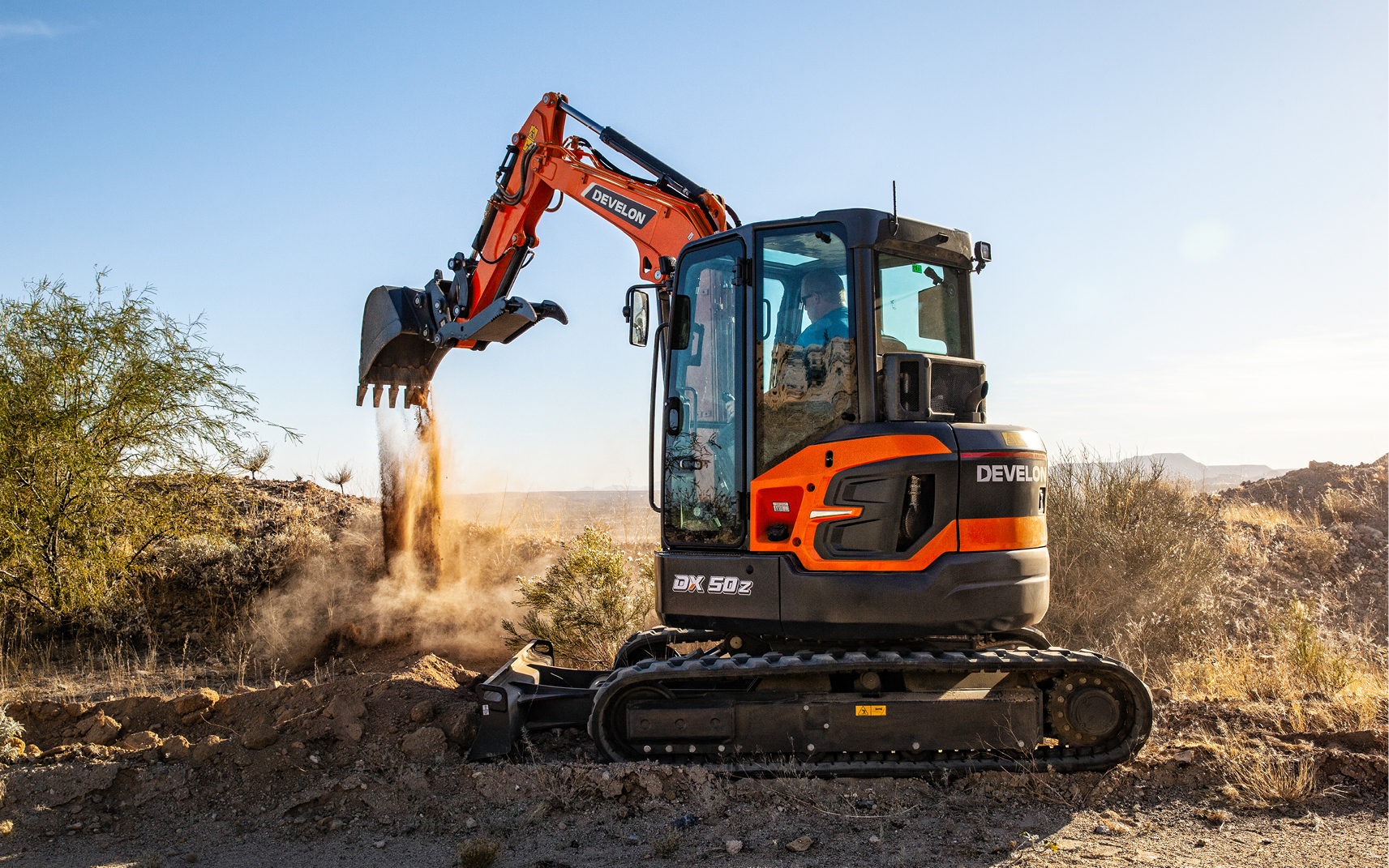 A DEVELON mini excavator unloading a pile of dirt at a job site.