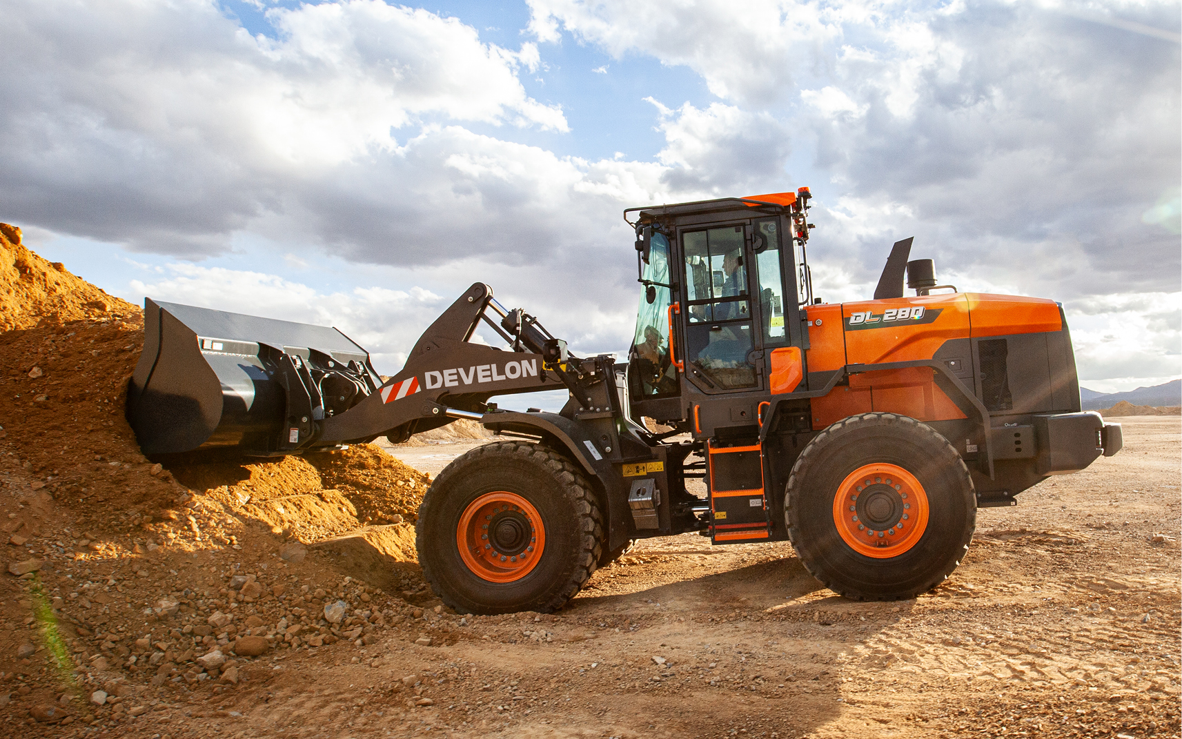 A DEVELON wheel loader scooping a pile of dirt into bucket.