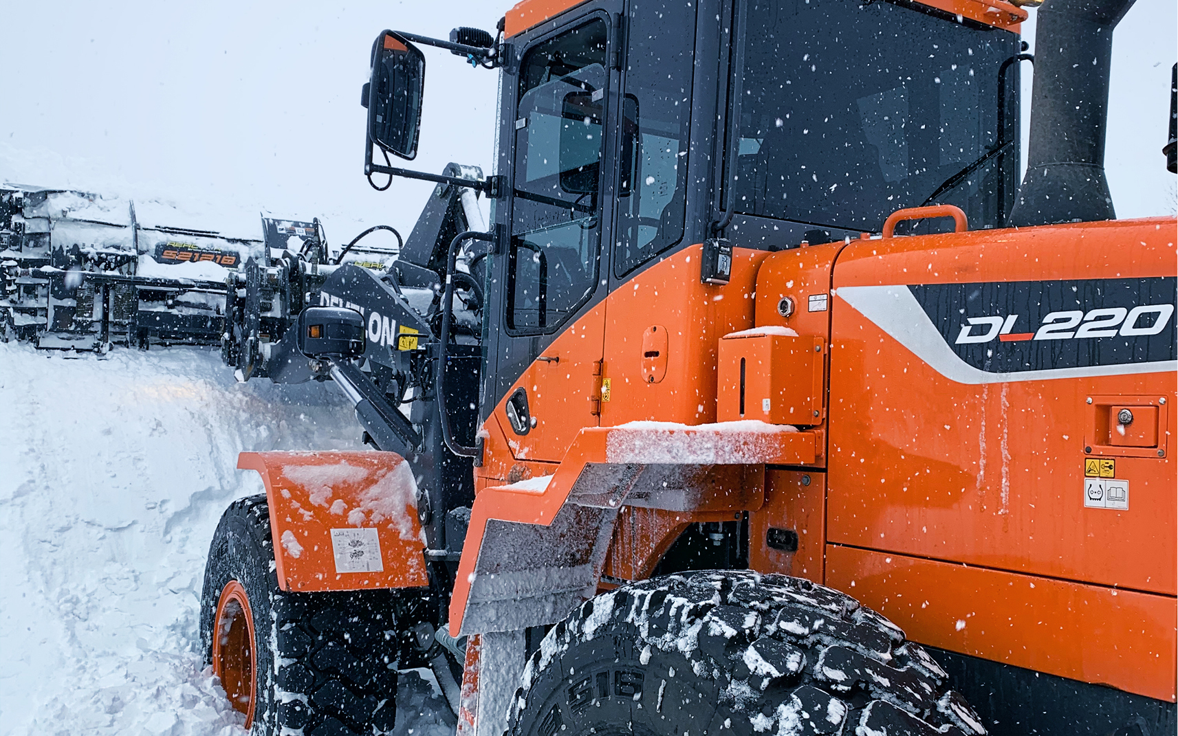 A DL220 wheel loader pushing snow using a snow pusher attachment.