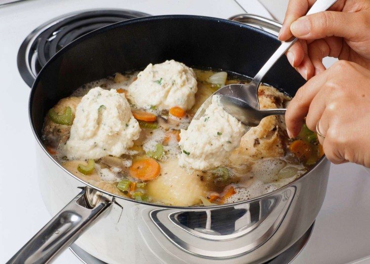 Spooning dumplings into pan of chicken and veggies