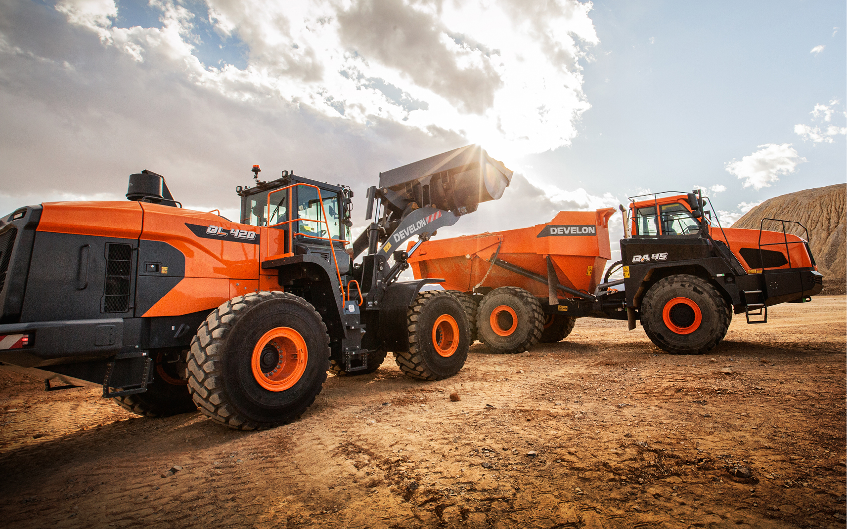 A DEVELON wheel loader dumping dirt into the back of an articulated dump truck. 