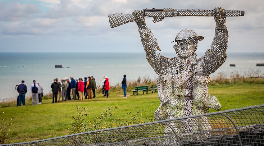 A soldier sculpture at the Arromanches D-Day Garden, with a group in the background