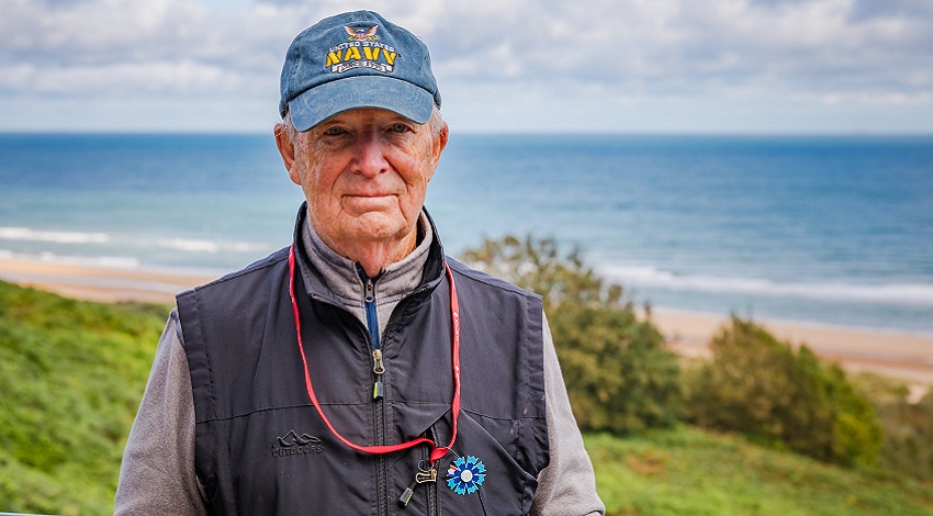 A Road Scholar stands in front of the ocean wearing his bleuet de France flower pin