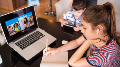 Student writing on paper in front of laptop