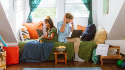 Students on couch eating popcorn watching laptops